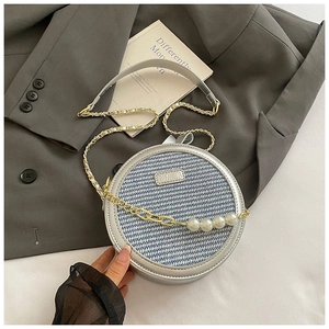 Détail d'un sac rond argenté avec panneaux rayés bleus et chaîne ornée de grosses perles