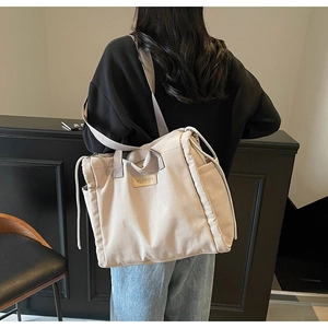 Detail showing leather brand patch and side drawstring pocket of beige canvas tote bag