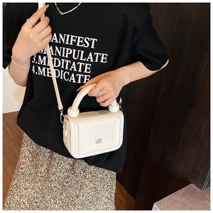 Close-up of white PU leather crossbody bag featuring lychee texture and ball handle detail
