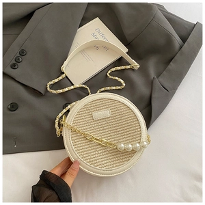 Détail du sac bandoulière rond en paille avec chaîne dorée, perles et bordure en cuir blanc