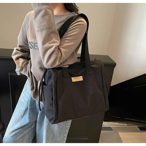 Detail of black nylon tote bag with beige leather logo and drawstring side accents