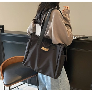 Detail of a large black canvas tote bag with brown leather logo patch and dual straps
