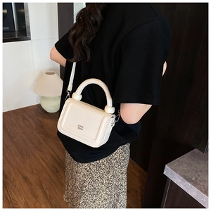 Detail showing white leather handbag with cylindrical top handle and metal buckle closure
