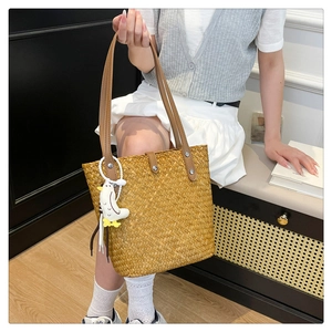 Detail of handwoven straw tote bag with brown leather straps and cute duck pendant decoration
