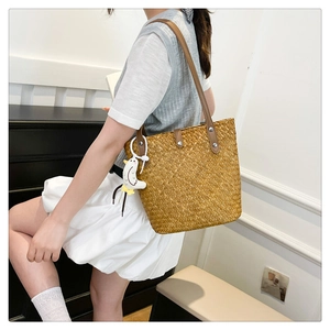 Detail of hand-woven straw tote with brown leather strap and cute duck pendant accessory