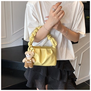 Detail view of light yellow pleated handbag with a cute brown bear plush accessory