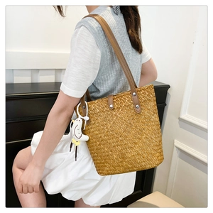 Detail view of straw tote bag with brown leather straps and white bird charm