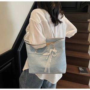 Detail of light blue textured tote bag featuring lace bow and pearl pendant on leather strap