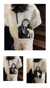 Detail of black glossy bucket bag with pearl heart pendant and lace bow accessory