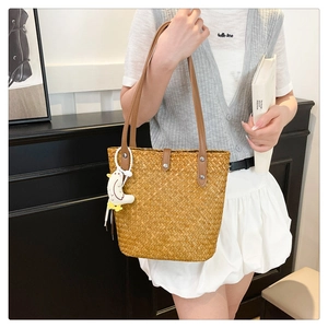 Detail of handmade straw tote bag with brown leather handles and bird charm accent