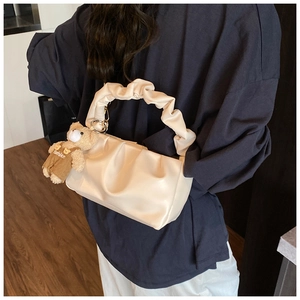 Detail of creamy white pleated cloud bag with a cute bear charm and gold chain accents