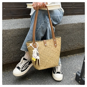 Detail of hand-woven straw tote bag with brown leather straps and plush chick charm accessory