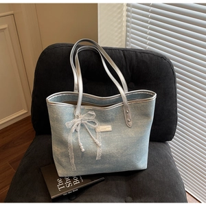 Detail of light blue denim tote with silver handles and pearl bow decor on a chair