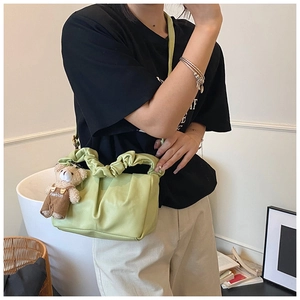 Close-up of a light green pleated cloud bag with a cute teddy bear charm accessory