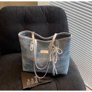 Detailed close-up of a blue denim tote bag with silver leather trim and a lace pearl bow