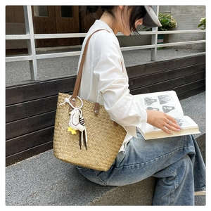 Detail of woven straw tote bag with brown leather straps and a cute plush chick pendant