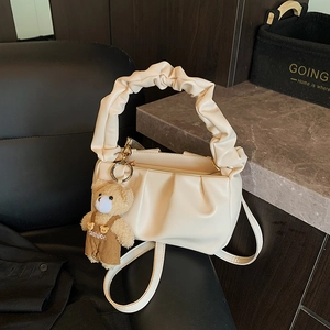 Close-up of beige pleated cloud bag with a cute teddy bear pendant on a black chair