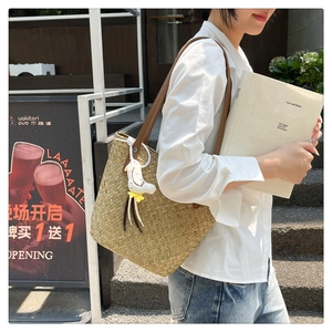 Detail of hand-woven straw tote bag with brown leather straps and a bird pendant