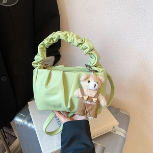 Detail of mint green pleated cloud bag with a cute teddy bear charm on white books
