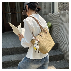 Detail of a straw tote bag with brown leather handles and a plush chick charm on street