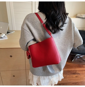 Close-up of red bucket bag with litchi grain texture and adjustable shoulder strap