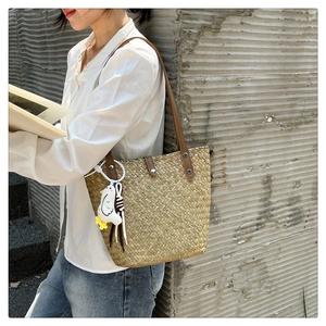 Close-up of handmade straw tote bag with brown leather straps and cute plush chick ornament