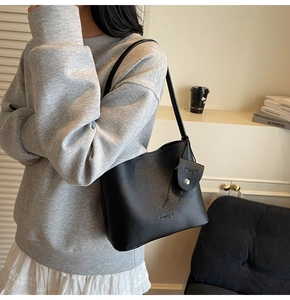 Detail of black lychee grain leather bucket bag with metallic buckle and hangtag decoration