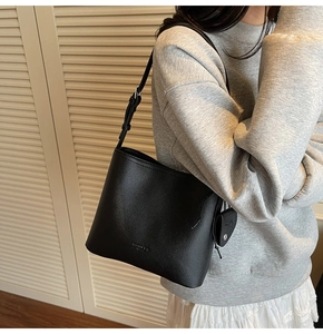 Detail of black lychee grain leather bucket bag with adjustable strap on a female model