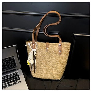 Close-up of straw tote bag with brown leather handles and cute plush chicken pendant