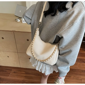 Detail of off-white lychee leather hobo bag with gold chain and strap in a lifestyle setting