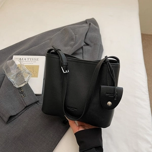 Detail of black pebbled leather bucket bag with adjustable strap and small coin purse charm