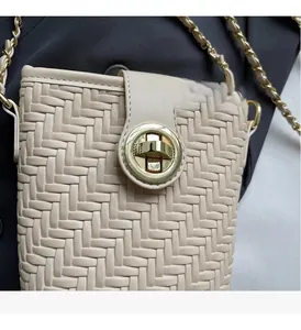 Détail du sac bandoulière tissé beige avec fermoir rotatif doré et bandoulière chaîne