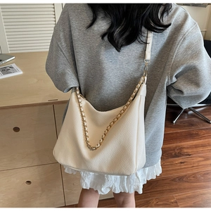 Close-up of beige lychee grain leather hobo bag with metal chain shoulder strap detail