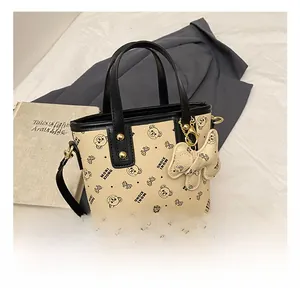 Detail of beige bucket bag with bear print, black handles, and cream bow pendant