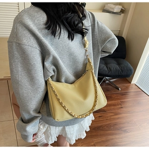 Detail view of a pale yellow hobo bag with litchi grain texture and a gold chain strap