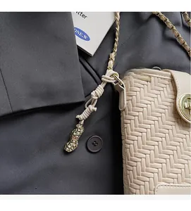 Détail du sac seau tissé beige avec pendentif cacahuète dorée et pompon en corde