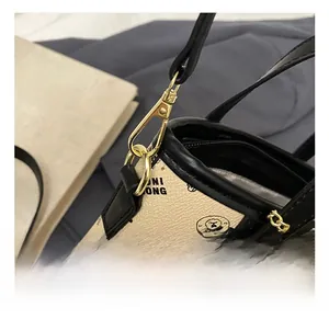 Detail of golden metal swivel hook and black leather strap on a beige litchi grain bag