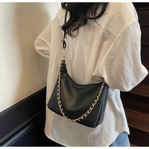 Detail of black pebbled leather dumpling bag with chunky gold chain and thin shoulder strap