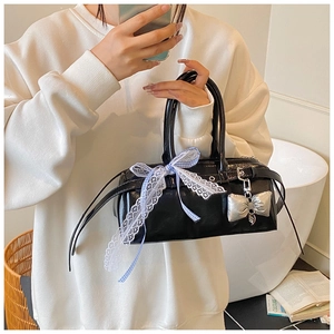 Détail du sac Boston en cuir verni noir avec ruban en dentelle et pendentif