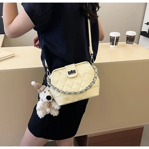 Detail of yellow quilted patent leather crossbody bag with silver chain and bear charm