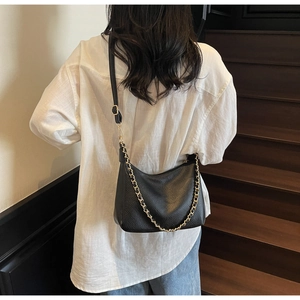 Detailed view of black lychee grain crossbody bag with a gold chain on a model