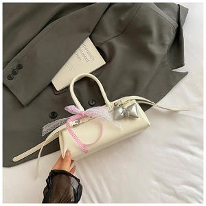 Détail du sac à main crème avec ruban en dentelle rose et breloque noeud argenté sur veste