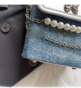Dettaglio della mini borsa in denim blu con fibbia a farfalla argento e catena di perle