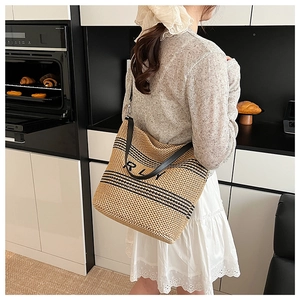 Détail du sac cabas en paille avec rayures noires, lanières en cuir et broderie RLY