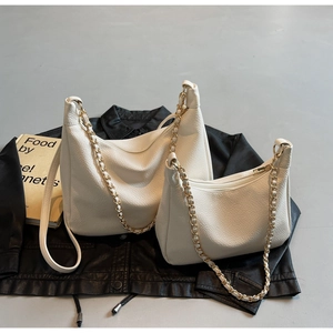 Detail of white lychee leather hobo bags with golden woven chains on black background