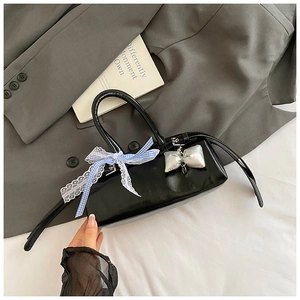 Détail du sac à main en cuir verni noir avec nœud à carreaux bleus et breloque argentée