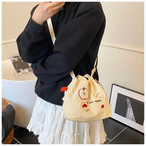 Dettaglio borsa a secchiello in tela beige con ricamo a mela rossa e tracolla sottile