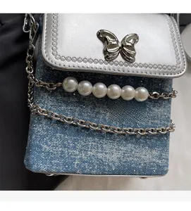 Dettaglio borsa porta cellulare in denim blu con fibbia a farfalla e catena di perle fini