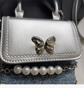 Dettaglio borsa a tracolla argento metallizzato con denim blu e tracolla di perle
