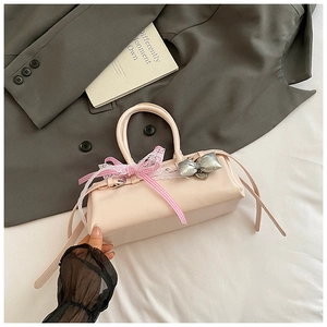 Détail du sac baguette rose clair avec bordures en dentelle et ornement de nœud à carreaux